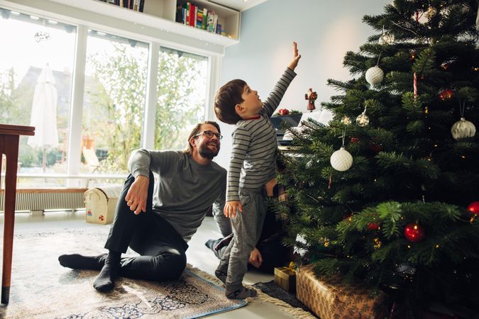 Small family together at home during Christmas with boy reaching up Christmas tree