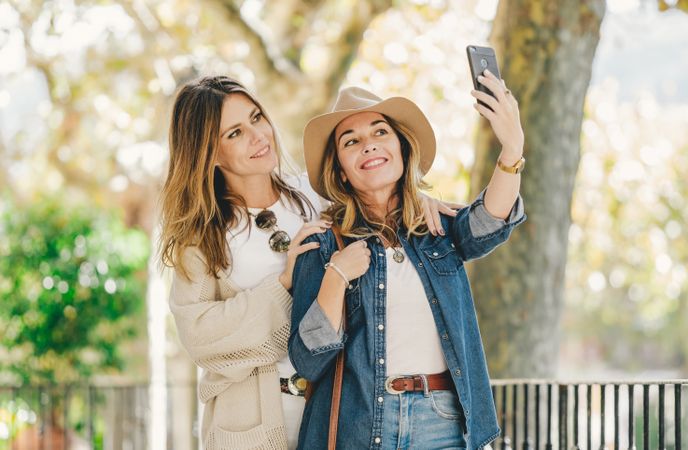 Smiling women taking selfie in street near cute tree