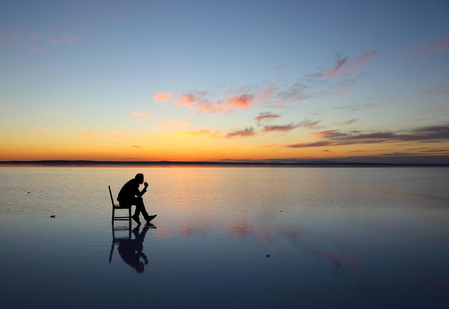 Silhouette of man sitting on chair on water