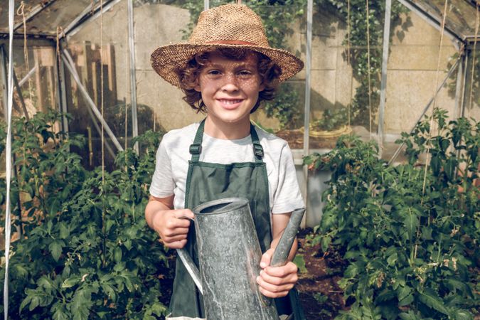 Cheerful preteen boy gardener with watering can in hothouse