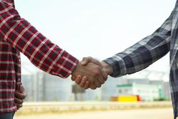 Businessmen shake hands against silos. Agriculture business
