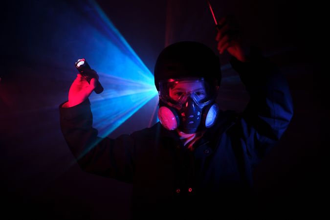 Robber in mask standing in darkness with flashlight