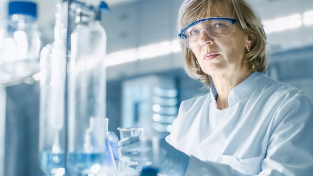 Mature Female Chemist in Safety Glasses Mixes Smoking Liquids in a Beakers.