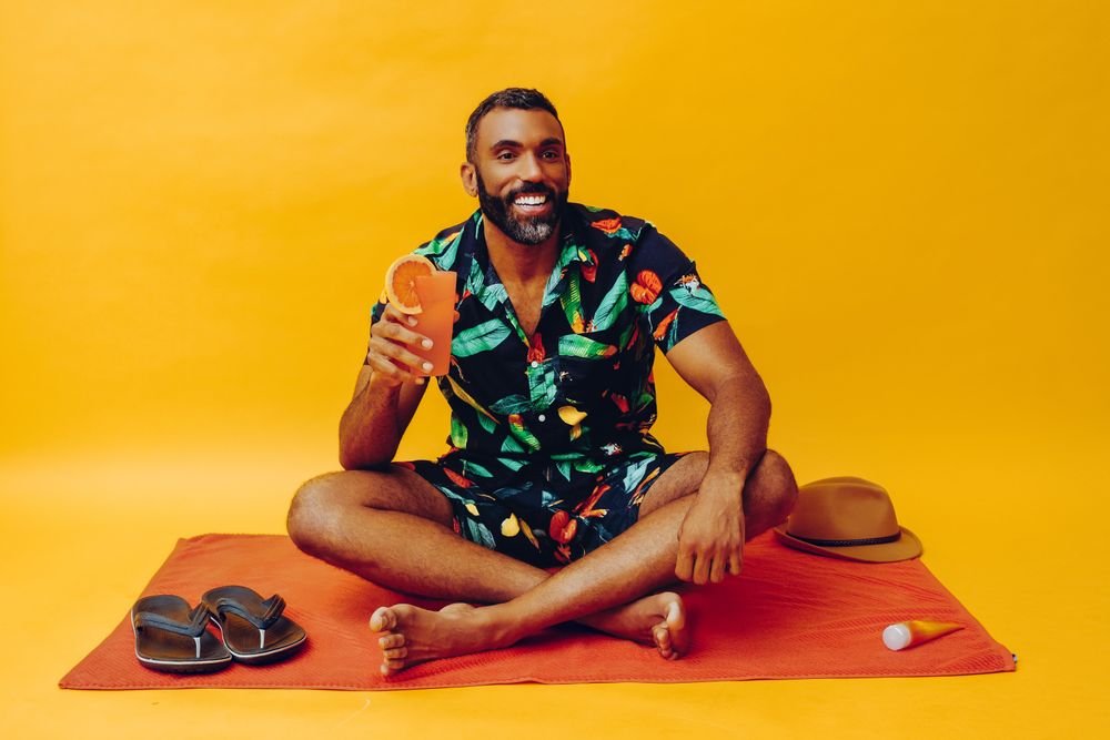 Black male sitting on towel and smiling while holding tropical drink