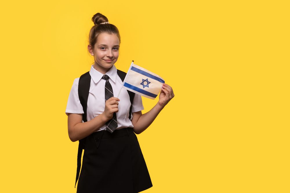 Schoolgirl proudly holds Israeli flag while smiling.