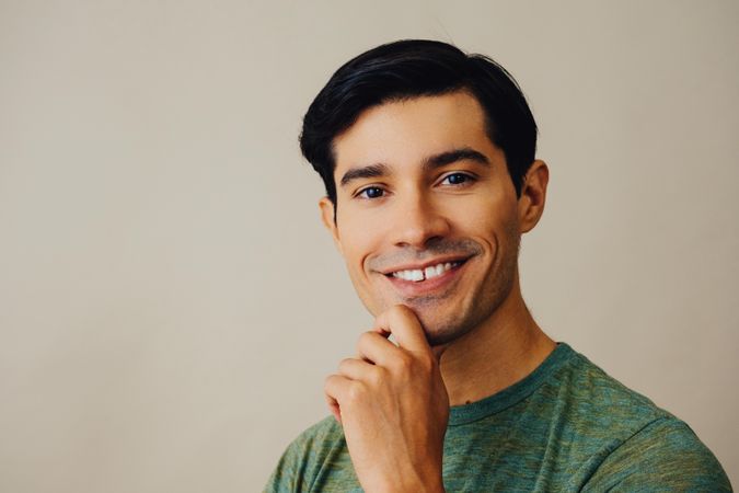 Headshot of happy Hispanic male holding his chin in neutral room