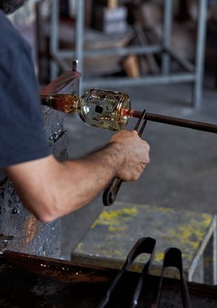 Crop glassblower shaping hot glass in workshop