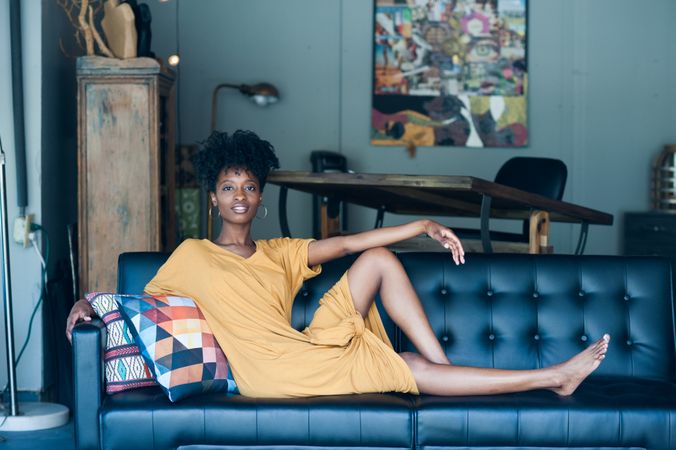 Young woman with curly hair and yellow dress sitting on couch