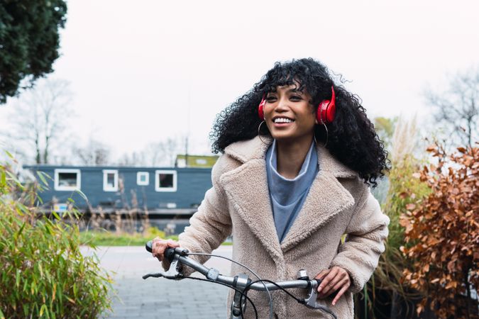Cheerful Black woman in headphones with bicycle