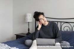 Young female thinking while sitting on her bed with a laptop 4mDje5