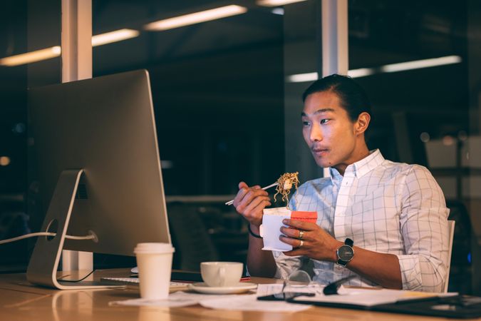 Entrepreneur working in office late in the night and eating noodles sitting at his desk