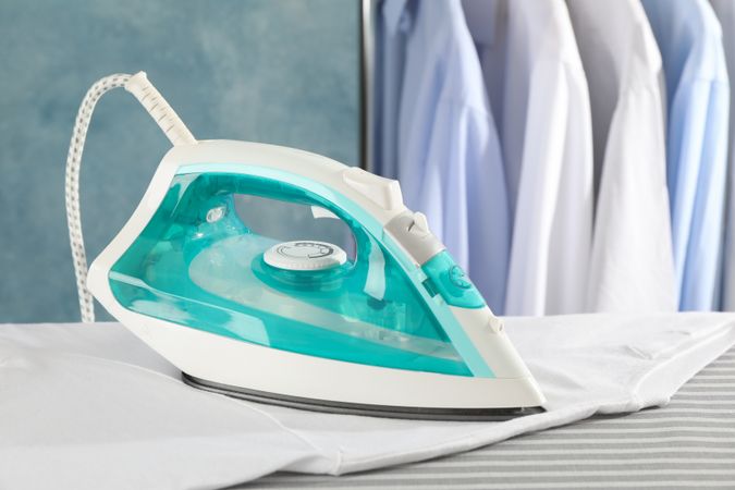 Iron and t-shirt on ironing board, space for text