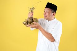 Asian Mature Man Wearing Shirt Baju Koko and Caps Kopyah Holding Ketupat Rice Cakes for Eid al Fitr