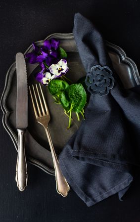 Top view of dark table setting for Easter dinner with delicate purple flowers
