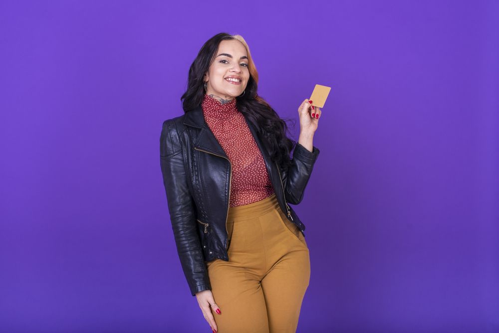 Woman showing a credit card on purple background. Shopping concept.
