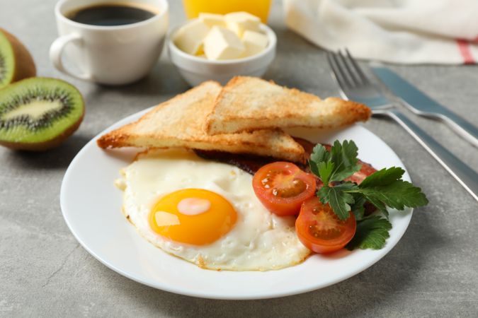 Breakfast plate of egg, tomatoes, toast and kiwi