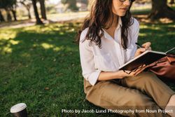 Woman sitting on grass at park with book making notes bDW7E4