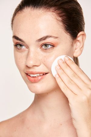 Peaceful female applying toner on radiant face with sponge