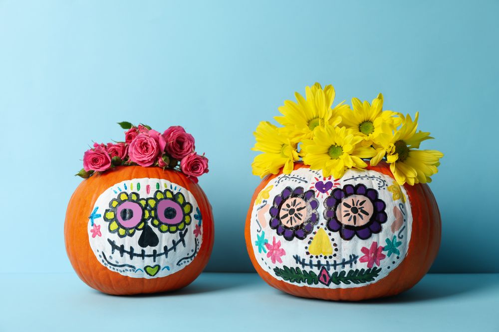 Pumpkins with catrina skull makeup and flowers on blue background