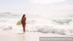 Woman holding surfboard walking out of the sea 439JO0