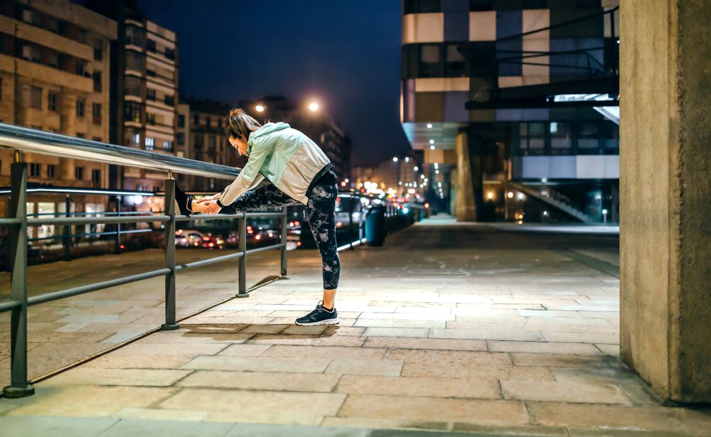 Side of woman stretching her legs over banister before training at night in town