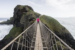 Woman crossing rope bridge leading to rocky island