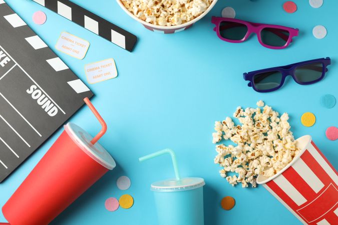 Flat lay composition with drinks, popcorn, 3d glasses, clapperboard, tickets on blue background, copy space