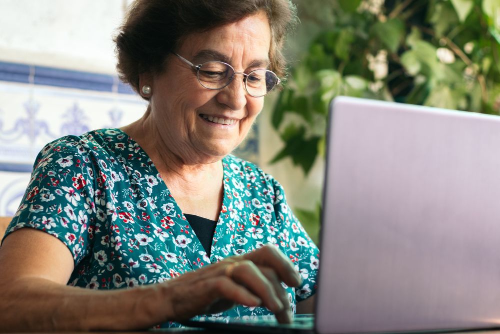 Mature woman with glasses using a laptop and a notebook at home
