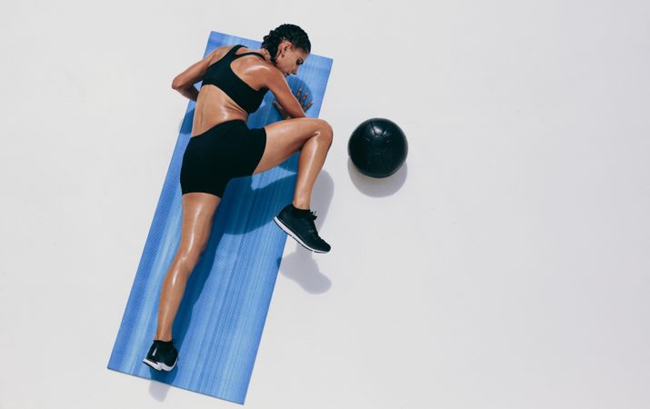 Athletic woman exercising on yoga mat with medicine ball beside her