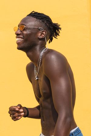 Cheerful man in trendy sunglasses posing near wall