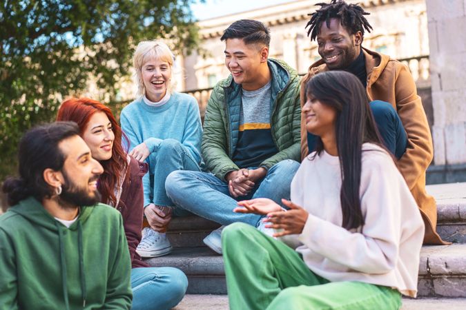 A diverse group of friends laugh and converse on sunny city steps, enjoying a lively discussion