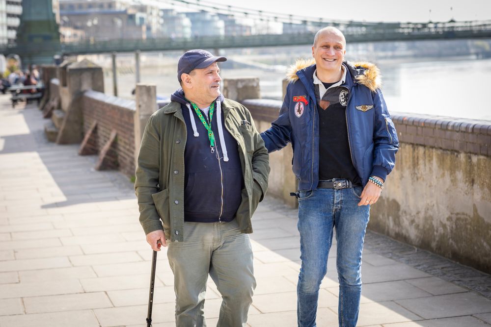 Two smiling male friends walking by the river and talking