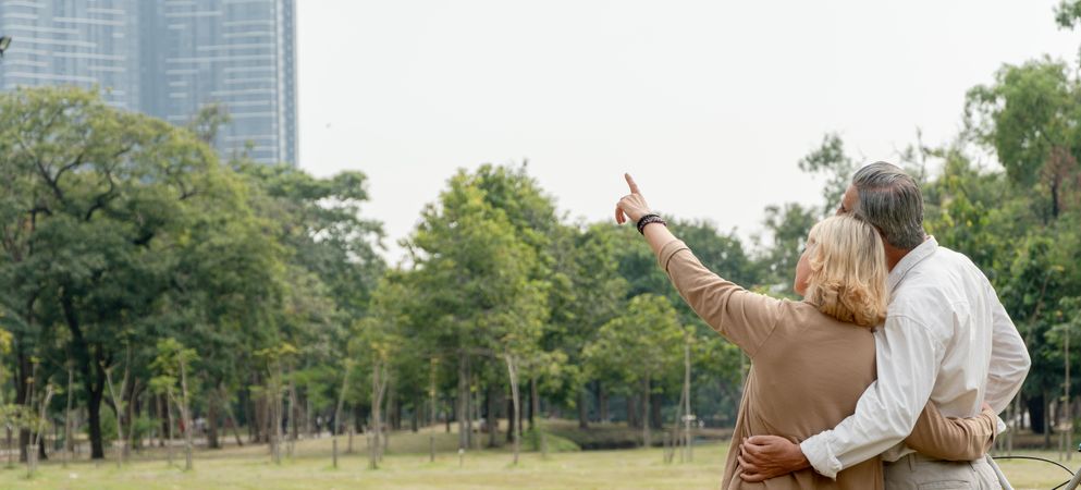 Wide shot of mature man and woman standing in park and pointing up