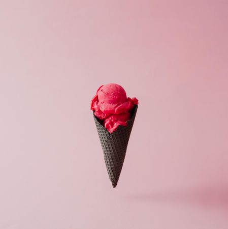 Strawberry ice cream in dark waffle cone on pink pastel background