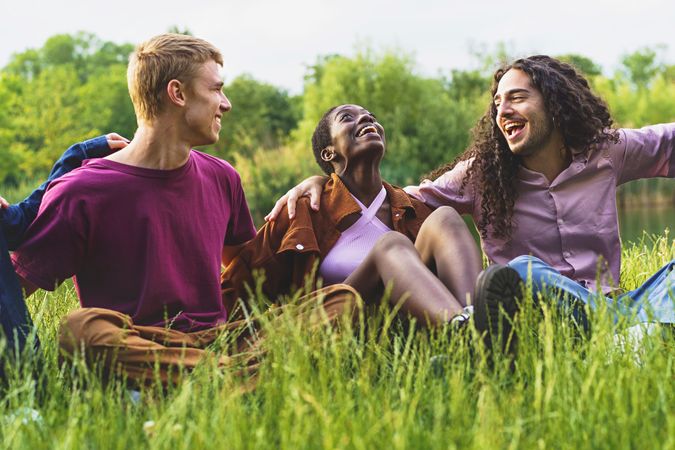 Cheerful multiethnic friends bonding and having fun hugging and laughing on the grass