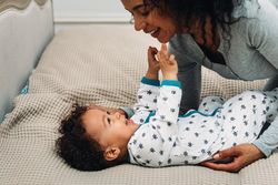 Smiling mother playing with toddler lying on bed