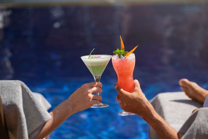 Crop woman and man clinking glasses of cocktails in poolside