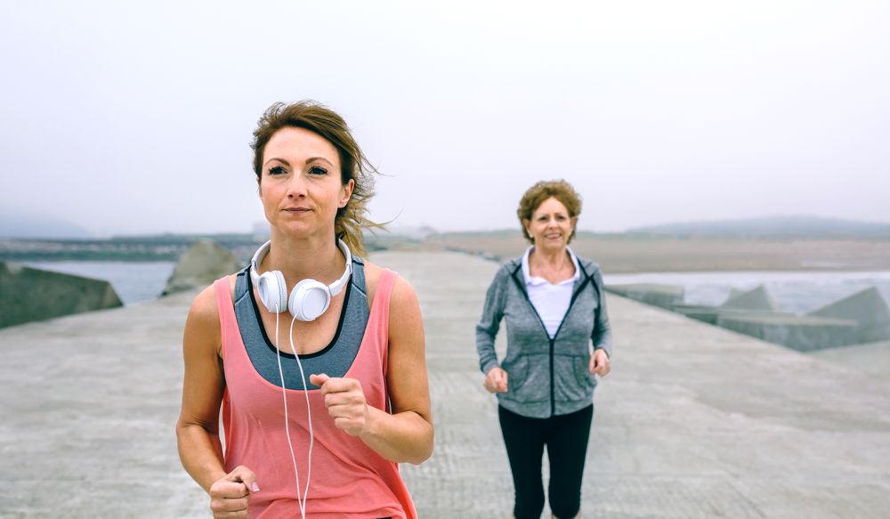 Older mother and daughter running by sea pier