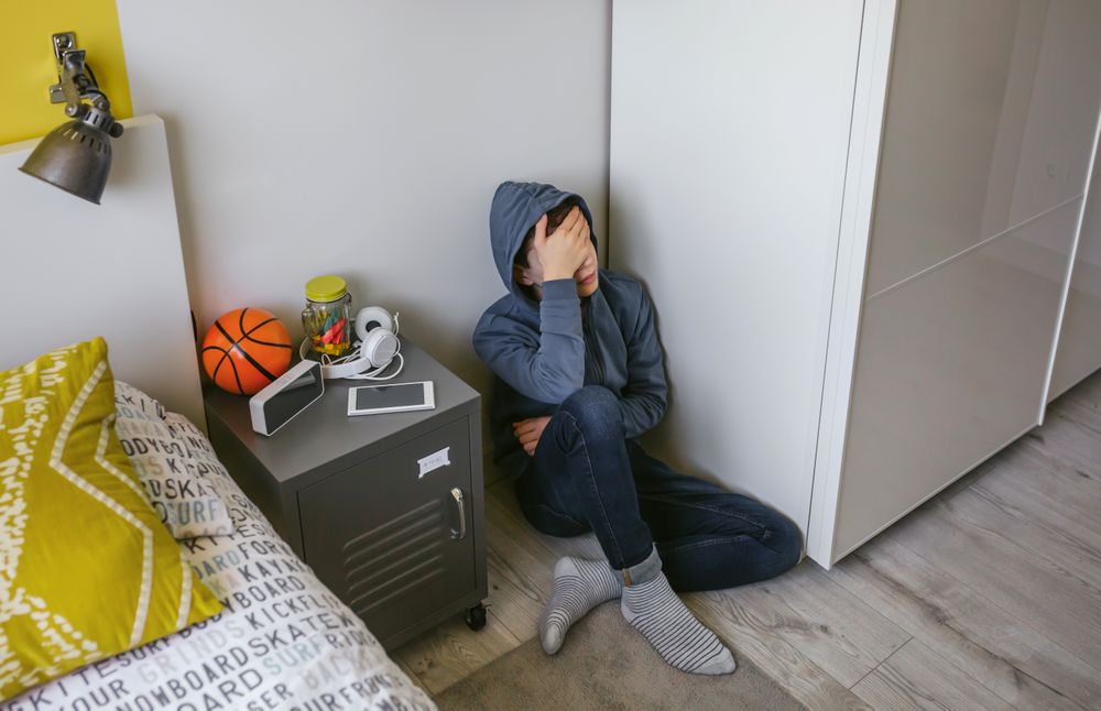 Depressed male teenager sitting on the floor in his bedroom