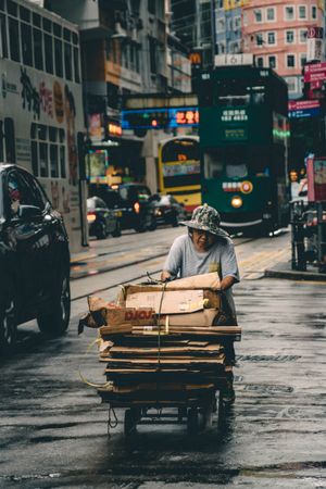 Older woman pushing a cart of sorted cardboards on the road in the city