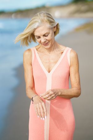 Older woman looking down at her wrist while walking along coast, vertical
