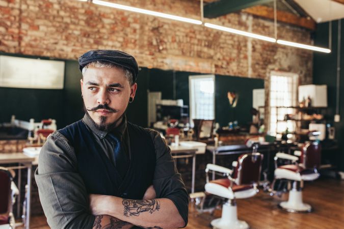 Stylish hairdresser standing with arms crossed in barbershop