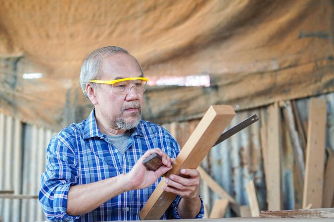 Asian male carpenter using ruler on wooden plank