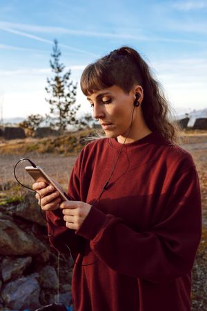 Young woman with piercing listening music on smartphone on hill
