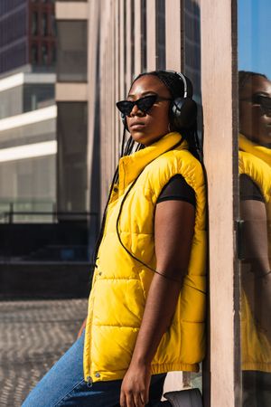 Black woman listening to music while leaning on a wall