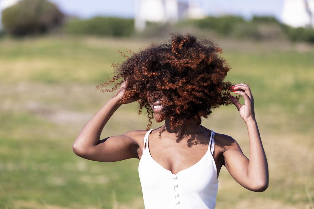 Female pictured outside in park playing with her curly hair in the wind