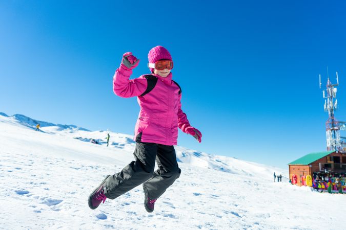 Child in pink snow suit jumping for joy on snowy hill