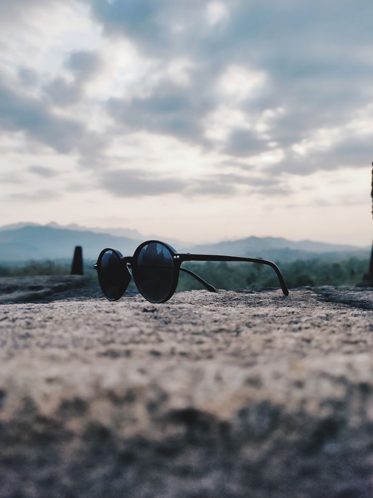 Sunglasses Resting on a Stone Wall with Mountain and Sky Background: A Serene Landscape