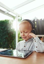 Blond boy using headphones and watching show on digital tablet