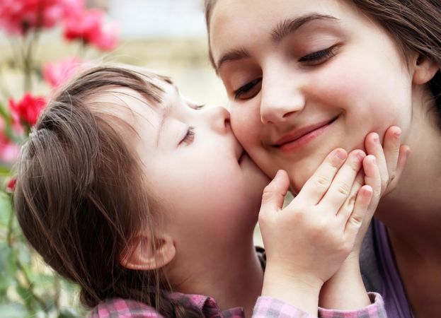 Young girl giving big sister a kiss on cheek